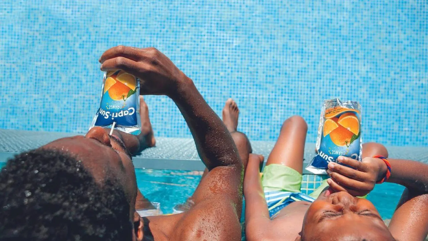 Children enjoying Capri Sun beside a pool on a sunny day